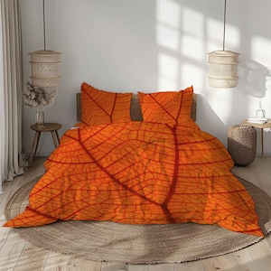 May include: An orange and red leaf-patterned bedding set. The set includes a duvet cover and two pillowcases, all featuring a detailed leaf vein design. The bed is made up with a round, brown rug.