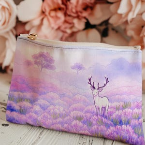 May include: A rectangular canvas pouch with a zipper closure and a gold-colored pull. The pouch features a watercolor painting of a white deer with purple antlers standing in a field of lavender flowers under a cloudy sky.