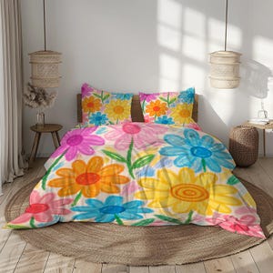 Puede incluir: Un juego de cama floral colorido con una funda nórdica y dos fundas de almohada. El diseño presenta grandes flores dibujadas a mano en tonos de rosa, naranja, amarillo y azul sobre un fondo blanco. Los tallos y hojas verdes completan el aspecto artístico.