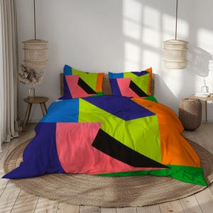 Può includere: Un set di biancheria da letto colorato con un design geometrico. La biancheria da letto comprende un copripiumino e federe con grandi blocchi di blu, verde, arancione, rosa e nero. Il letto è su un tappeto rotondo tessuto.