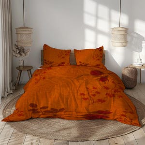 Puede incluir: Un juego de cama que incluye una funda nórdica y dos fundas de almohada a juego en un vibrante color naranja quemado. La tela está decorada con un estampado botánico rojo oscuro de tallos florales, hojas y motivos de capullos de rosa.