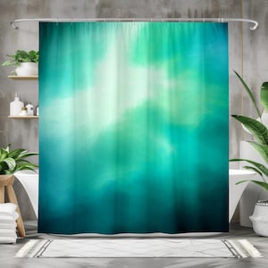 Op de afbeelding: Een turquoise en blauwgroen douchegordijn met een aquarelachtig ontwerp. Het gordijn heeft een gradiënteffect, van donker turquoise aan de onderkant naar lichter turquoise en wit aan de bovenkant. Het ontwerp creëert een zacht, vervaagd effect.