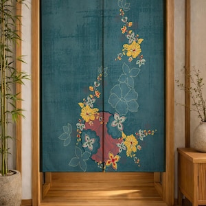 Op de afbeelding: Een blauwgroen stoffen noren-gordijn met een verticale rangschikking van gele hibiscusbloemen, rode cirkelvormige accenten en witte geborduurde bloemcontouren. Het textiel heeft een getextureerd, verweerd uiterlijk en is in het midden gespleten.