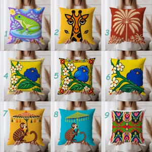 May include: A collection of nine square throw pillows featuring various graphic designs including a green frog, a giraffe, a palm tree, blue birds on branches, monkeys holding umbrellas, and a colorful symmetrical floral pattern.