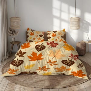 May include: Beige bedspread and pillowcases with a repeating pattern of autumn leaves in shades of orange, brown, and yellow. The leaves are various shapes and sizes, creating a fall-themed bedding set.