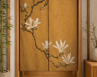 Puede incluir: Una cortina noren rectangular de tela con fondo amarillo mostaza y una ilustración impresa de flores de magnolia blancas sobre ramas de color marrón oscuro. La cortina está dividida verticalmente por el centro y cuelga de un marco de madera.