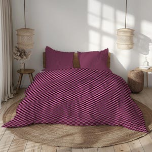 May include: A bed with a pink and black checkered pattern duvet cover and two matching pillowcases. The bed is made up with a wooden headboard and sits on a round, woven rug. The room has a neutral color palette.