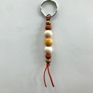 May include: A wooden bead keychain with a silver key ring. The beads are brown, white, and yellow. The keychain has a brown leather cord.