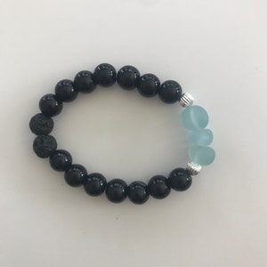 May include: A black beaded bracelet with a lava rock bead and three light blue glass beads.
