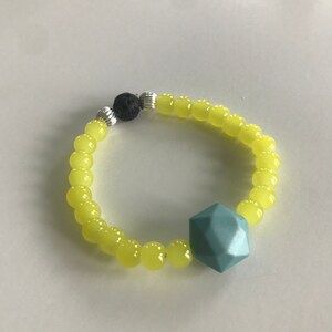 May include: A yellow beaded bracelet with a teal geometric charm and a black lava bead.