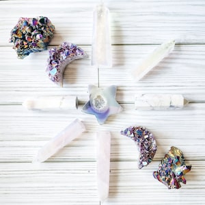 May include: A collection of iridescent crystals in various shapes, including a star, crescent moon, and points. The crystals are arranged on a white wooden surface.