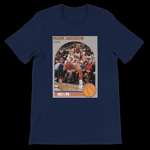 May include: Navy blue t-shirt featuring a basketball card graphic. The card shows Mark Jackson, a guard, in action with a basketball. The word "HOOPS" is printed at the bottom, and an orange basketball graphic is also included.