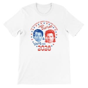 以下が含まれることがあります： 2つの顔と「Jack Burton & Wang Chi 2028」の文字が特徴の白いTシャツ。デザインには「May the wings of liberty never lose a feather」というフレーズと赤と青の星が含まれています。