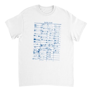 May include: White t-shirt featuring a blue library card print. The design includes the text "DATE DUE" and handwritten dates and notes in a grid format. A vintage-inspired design.