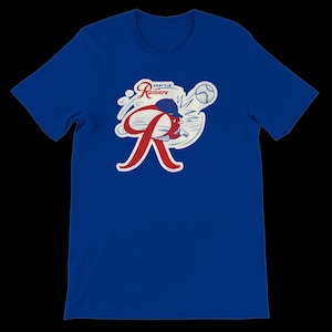 May include: Royal blue t-shirt with a retro Seattle Rainiers baseball team logo. The design features a red 'R', a baseball, and a cap, with the words 'Seattle Rainiers' in a vintage style.