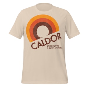 Op de afbeelding: Crèmekleurig T-shirt met een retro design. Het heeft een cirkelvormige afbeelding in oranje en bruine tinten. Het woord "CALDOR" is diagonaal gedrukt, met de zin "WHERE SHOPPING IS ALWAYS A PLEASURE" eronder.