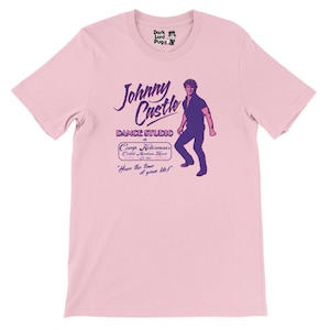 May include: Light pink t-shirt featuring a purple graphic of a man and text that reads "Johnny Castle Dance Studio" and "Camp Kellerman's". The shirt also has the phrase "Have the time of your life!"