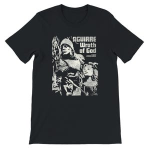 May include: Black t-shirt featuring a white graphic from the film "Aguirre, Wrath of God." The design includes a portrait of a man in armor and a woman, with the film's title in a textured font. A film by Werner Herzog.