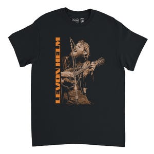 May include: Black t-shirt with a sepia-toned image of a musician playing a mandolin and singing. The text "LEVON HELM" is printed vertically in orange. The shirt has a crew neck and short sleeves. A Dark Star logo is visible on the upper right.