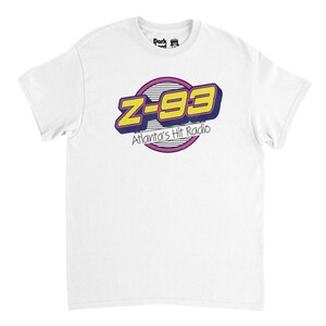 Peut inclure: T-shirt blanc avec le logo Z-93 Atlanta's Hit Radio en jaune, violet et rose. Le logo est de style rétro, avec un effet d'ombre. Le t-shirt est fait d'une matière douce.