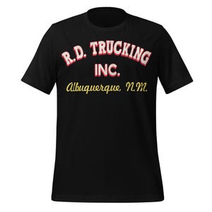 May include: Black t-shirt featuring the text "R.D. Trucking INC. Albuquerque, N.M." in a vintage style. The text is in red and white, with the city and state in yellow. The shirt is short-sleeved.