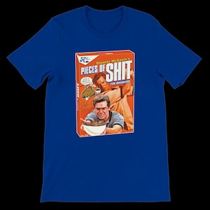 May include: Royal blue t-shirt featuring a graphic of a cereal box parody with the text "Shooter McGavin's Pieces of Shit for Breakfast." The box art depicts two men and a bowl of cereal. The shirt is a short-sleeved crew neck.