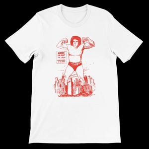 May include: White t-shirt with a red graphic of Andre the Giant flexing. The illustration includes the text "Andre the Giant" and his height and weight. The wrestler is shown above a city skyline.