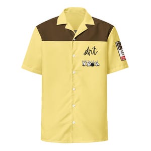 May include: Yellow short-sleeved shirt with a brown yoke. The shirt features the word "Art" in cursive, a bowling pin and ball graphic, and a patch on the sleeve. The shirt has a classic bowling shirt design.