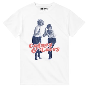May include: White t-shirt with a retro image of two women holding guns, and the text "Cagney & Lacey" in red and blue. The tee has a classic crew neck and short sleeves, suitable for everyday wear.