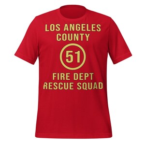 May include: A red t-shirt with the text "LOS ANGELES COUNTY" above a circle with the number "51" inside, and "FIRE DEPT RESCUE SQUAD" below. The text and circle are in a gold color.
