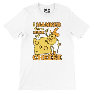 May include: White t-shirt with a cartoon cheese character in a cowboy hat and boots, holding a cane, next to a cheese block. The text says "I HANKER for a HUNK of CHEESE".