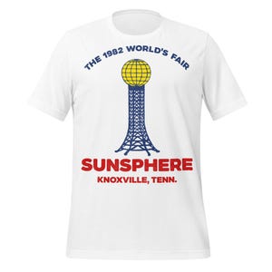 Puede incluir: Camiseta blanca con un gráfico de la Sunsphere de la Feria Mundial de 1982 en Knoxville, Tennessee. El diseño incluye el texto "THE 1982 WORLD'S FAIR" encima de la Sunsphere y "SUNSPHERE KNOXVILLE, TENN." debajo.