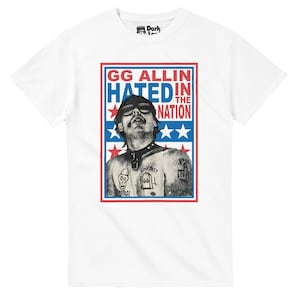 Puede incluir: Camiseta blanca con un gráfico de un hombre con gafas de sol y tatuajes, con el texto "GG ALLIN HATED IN THE NATION" en un diseño rojo, blanco y azul. La camiseta tiene cuello redondo y mangas cortas.