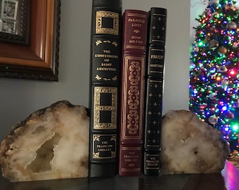 May include: Three hardback books with gold lettering and decorative designs on the spines are used as bookends. The bookends are made of a natural, light brown and white agate stone with a large, hollowed-out centre. The books are titled "The Confessions of Saint Augustine", "Paradise Lost" by John Milton, and "Faust" by Goethe. The books are part of "The Franklin Library" collection.