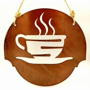May include: A brown metal sign with a white silhouette of a coffee cup and steam. The sign is oval shaped and has a rope hanger.