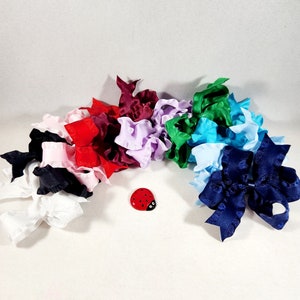 May include: A collection of colorful, ruffled fabric bows in various shades of red, pink, blue, green, and black. A small red ladybug charm is in the center of the image.
