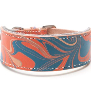 May include: A leather dog collar with a marbled pattern in shades of orange, blue, and beige. The collar has a silver buckle and white stitching.