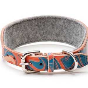 May include: A colorful leather dog collar with a blue and orange marbled pattern. The collar has a silver buckle and a gray felt lining.