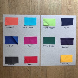 K&ouml;nnte beinhalten: Eine Farbkarte mit Stoffmustern in verschiedenen Farben, darunter Orange, Hellblau, Hellgr&uuml;n, Marineblau, Kobalt, Pink, Dunkelgr&uuml;n, Lila, Braun, Rot und Gelb. Die Farben sind unter jedem Muster beschriftet.