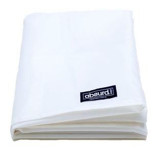 Puede incluir: Una sábana de tela blanca doblada con una etiqueta negra que dice "abeurd." La etiqueta tiene texto blanco que dice "Handmade in the UK."