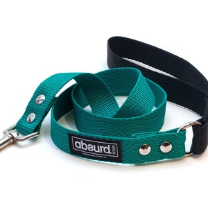 K&ouml;nnte beinhalten: Eine tealblaue Hundeleine mit schwarzem Griff und silbernem Karabiner. Die Leine hat ein schwarzes Etikett mit dem aufgedruckten Wort "abeurd".