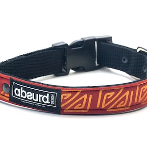 May include: Red dog collar with a black adjustable buckle and a gold geometric pattern. The collar has the text "abeurd design" printed on it.