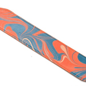 May include: A blue and orange marbled leather camera strap. The strap is made of a soft, supple leather and has a unique marbled design.