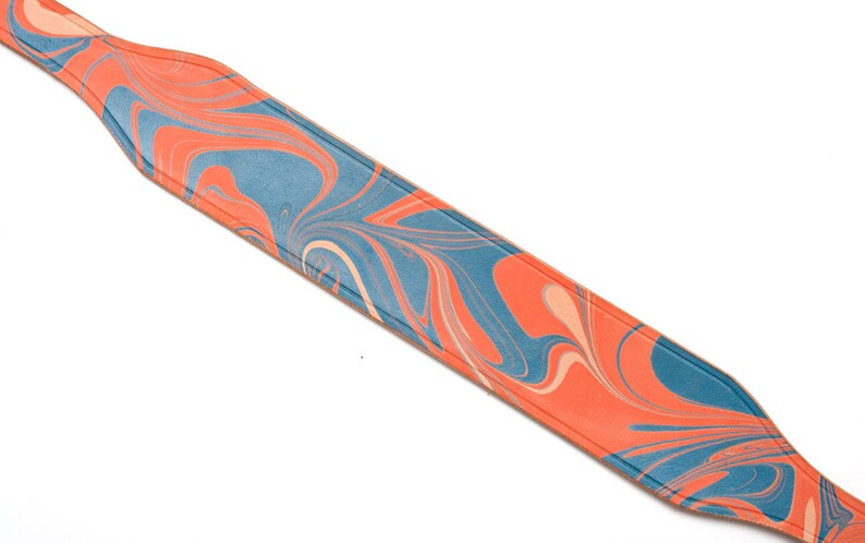 May include: A blue and orange marbled leather camera strap. The strap is made of a soft, supple leather and has a unique marbled design.