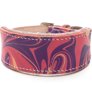 May include: A wide dog collar with a marbled pattern in shades of red, purple, and tan. The leather collar is stitched with white thread and has a metal buckle. The collar is designed for a pet.