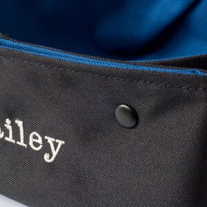 K&ouml;nnte beinhalten: Ein schwarzer Canvas-Aufbewahrungskorb mit blauer Innenausstattung und einem wei&szlig;en gestickten Namen "Bailey".