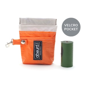 May include: An orange and white pouch with a silver metal clip and a black label reading abeurd design handmade in the uk. A grey circle with the text VELCRO POCKET is positioned above a green cylindrical roll of plastic waste bags.