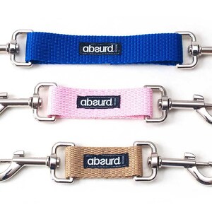 May include: Three dog leash extenders with silver clips. The extenders are blue, pink, and brown with the word "abeurd" printed on each.