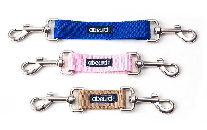 May include: Three dog leash extenders with silver clips. The extenders are blue, pink, and brown with the word "abeurd" printed on each.