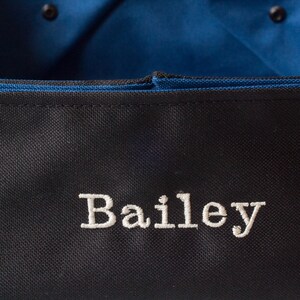K&ouml;nnte beinhalten: Schwarze Canvas-Tragetasche mit blauer Innenausstattung und dem Namen "Bailey" in wei&szlig; gestickt.